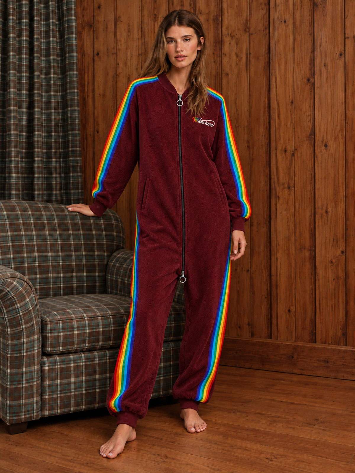 Adult model wearing a red rainbow-stripe onesie in a wood-panelled room