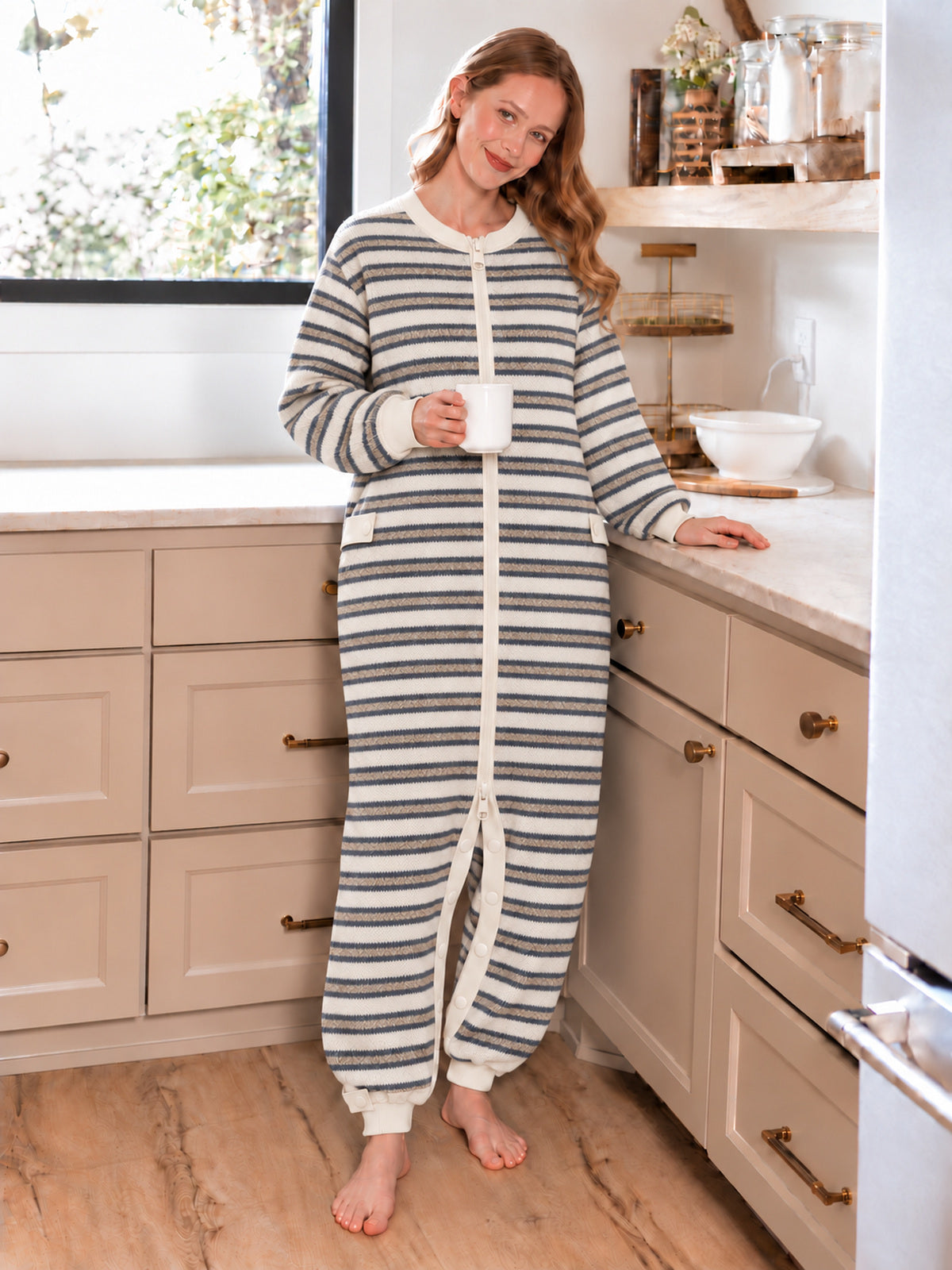 Adult model wearing the striped zip-front onesie while holding a mug in a kitchen