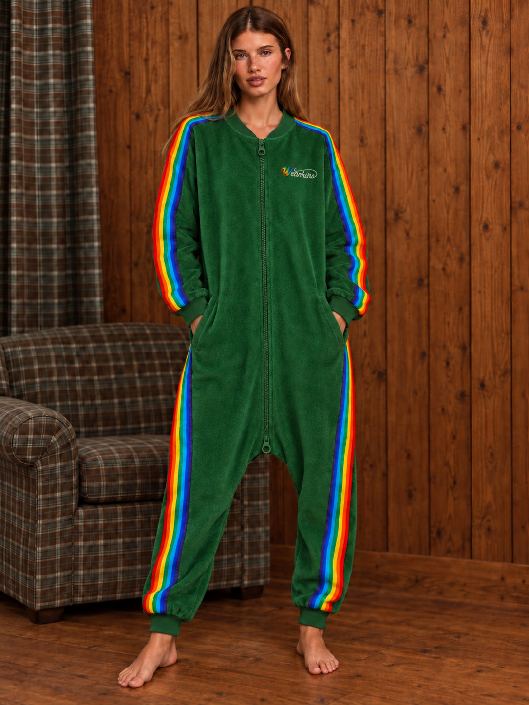 Adult woman wearing the forest green rainbow stripe terry onesie in a wooden living room