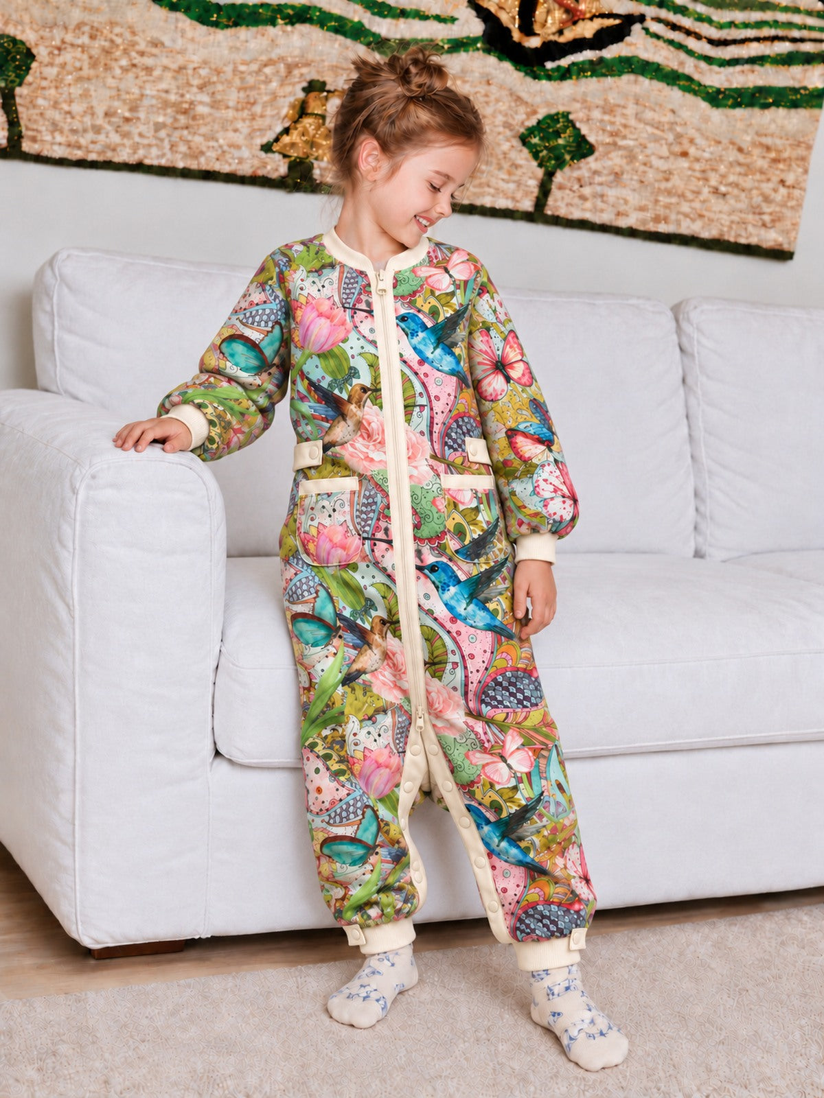 Child wearing the Hummingbird Garden floral onesie beside a sofa