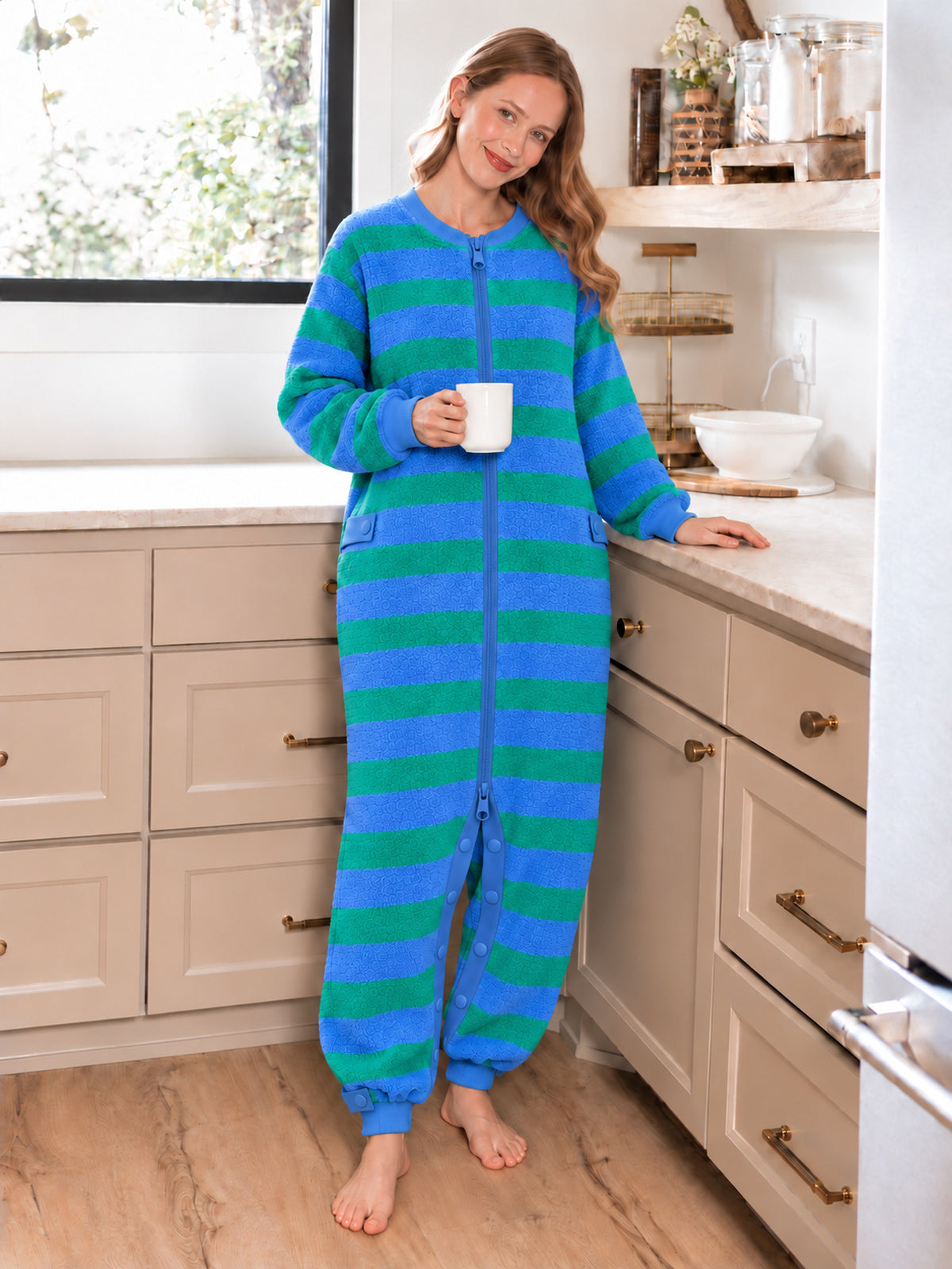Adult model wearing a blue-and-green striped terry onesie in a kitchen