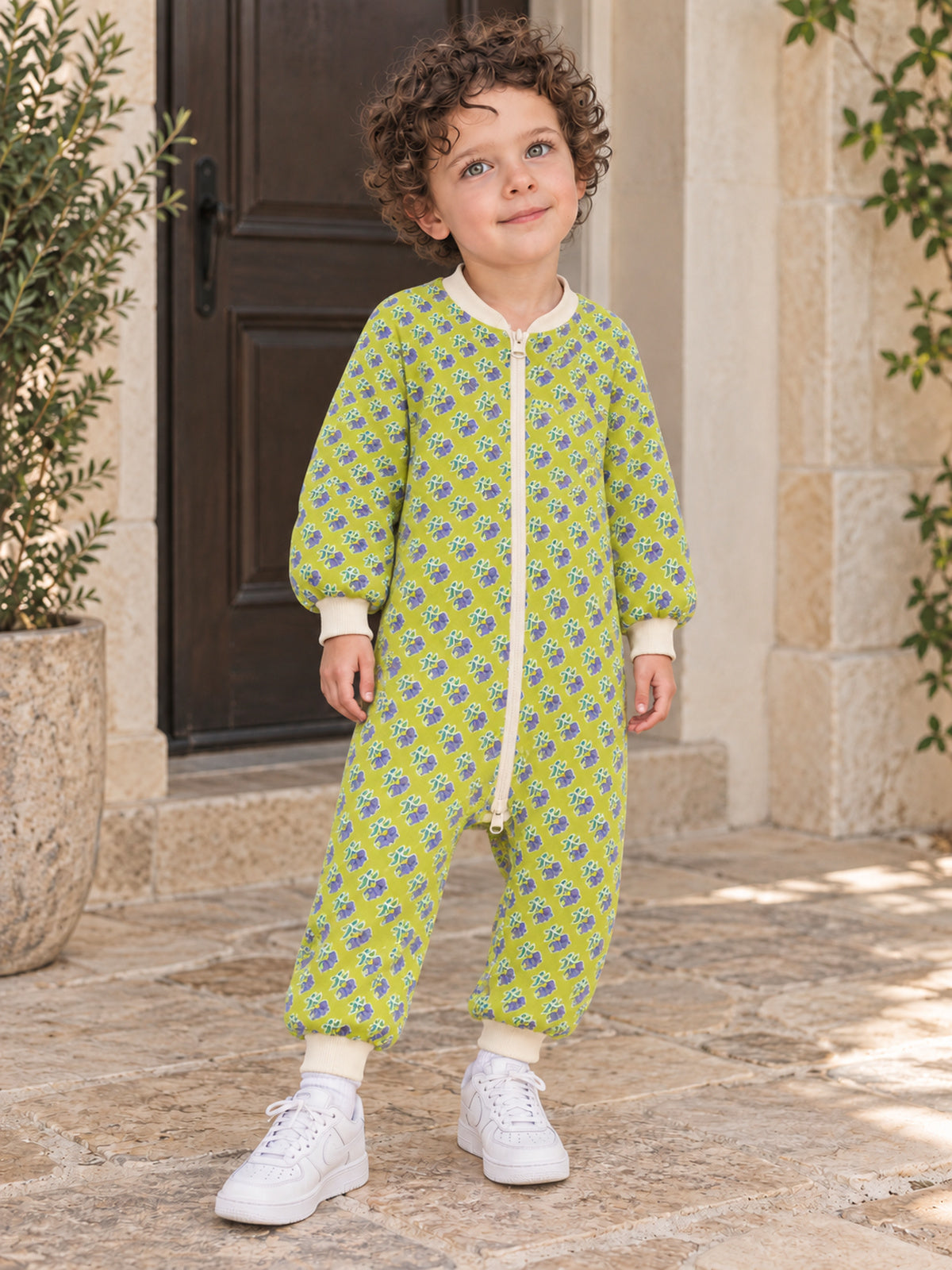 Boy wearing a lime-green floral onesie outside a doorway