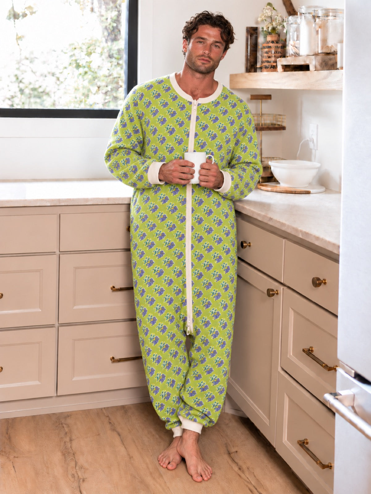 Adult man wearing a lime-green floral onesie while holding a mug in a kitchen