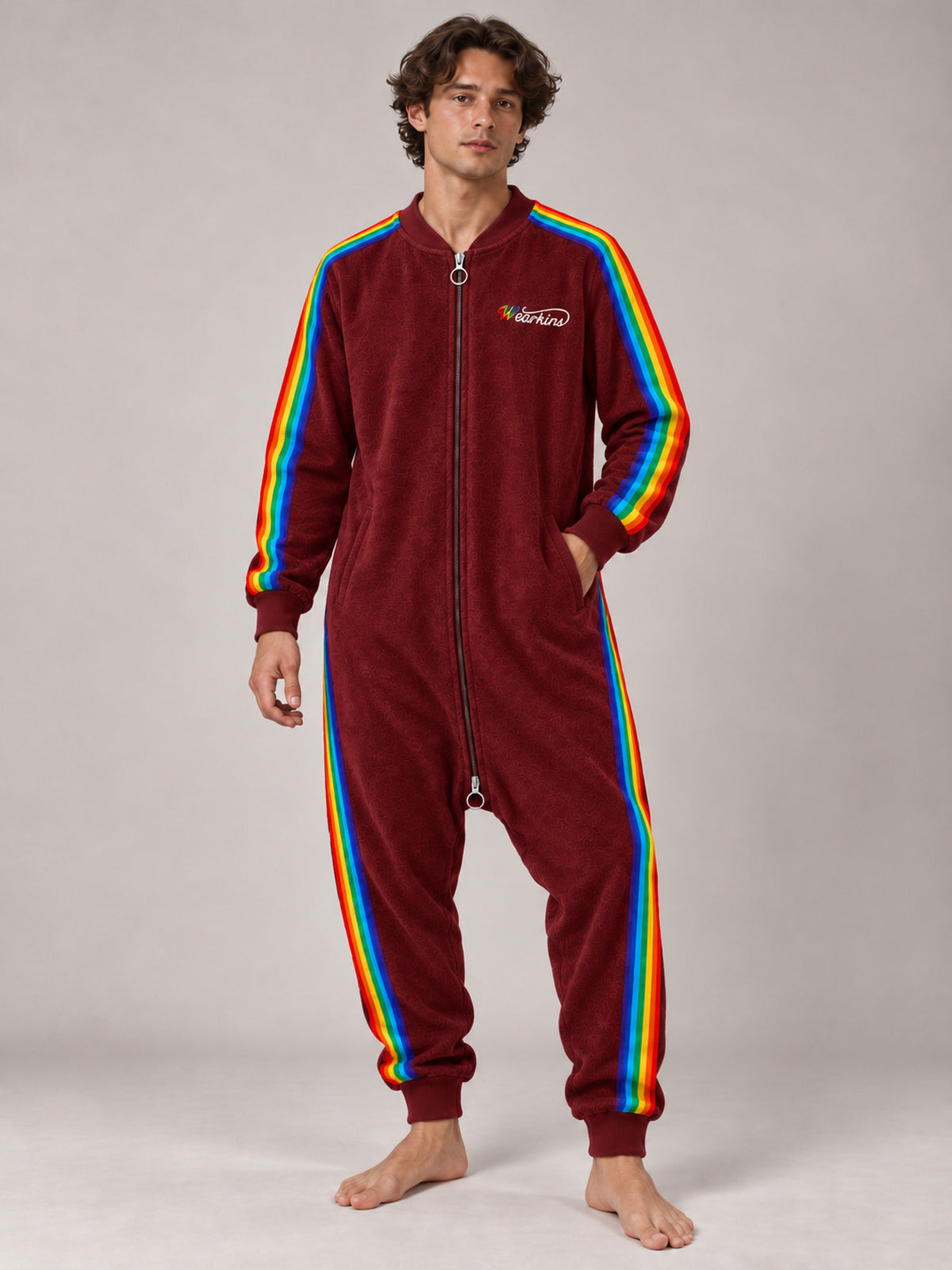 Adult model wearing a red rainbow-stripe zip-front onesie, front view