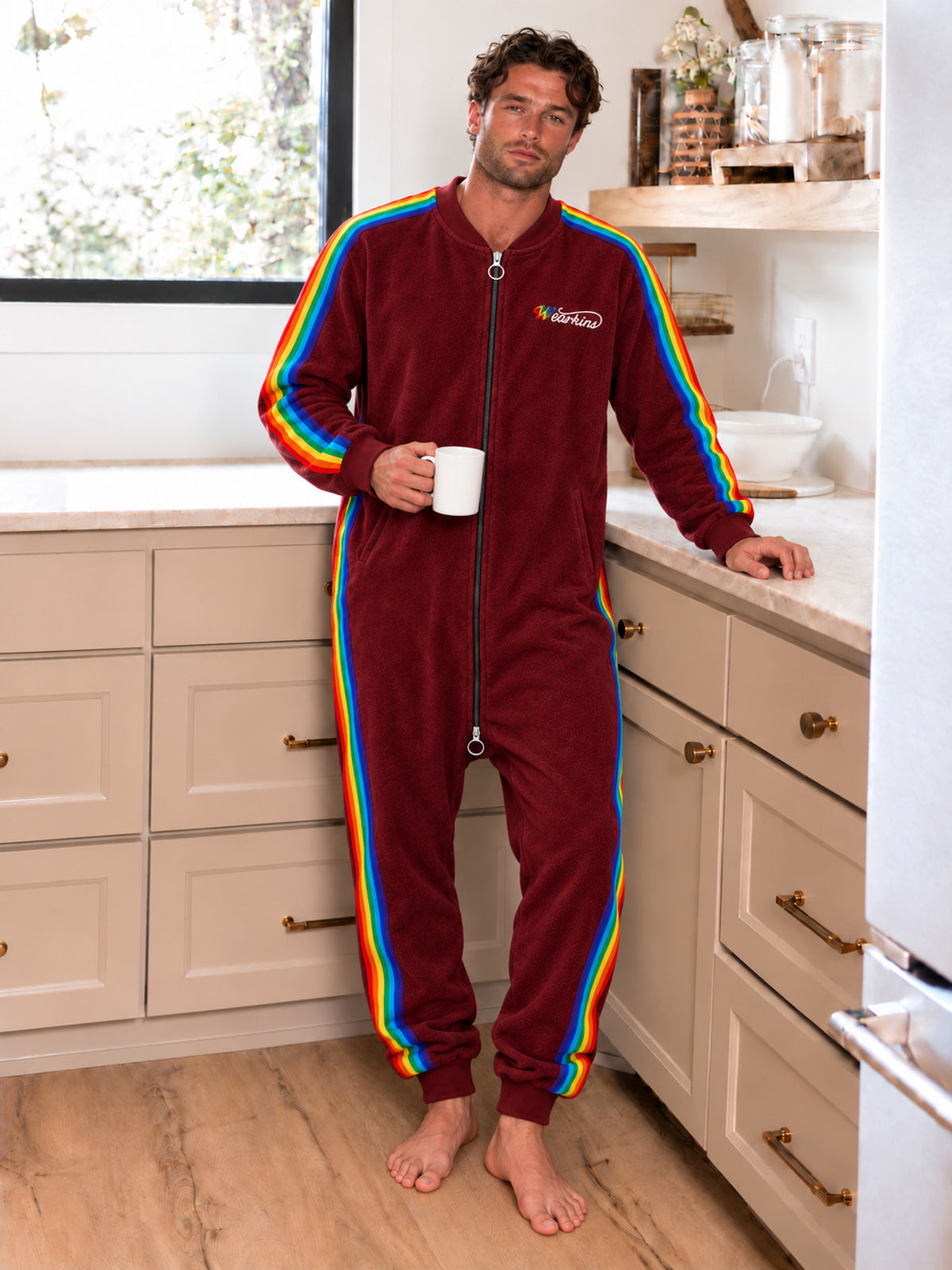 Adult model wearing a red rainbow-stripe onesie in a kitchen