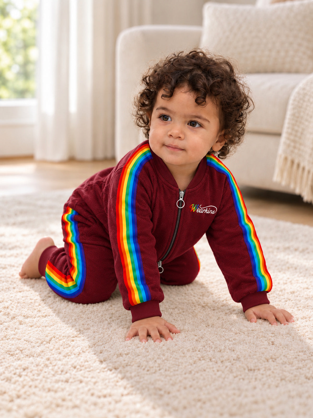 Baby wearing a red rainbow-stripe zip-front onesie while crawling indoors