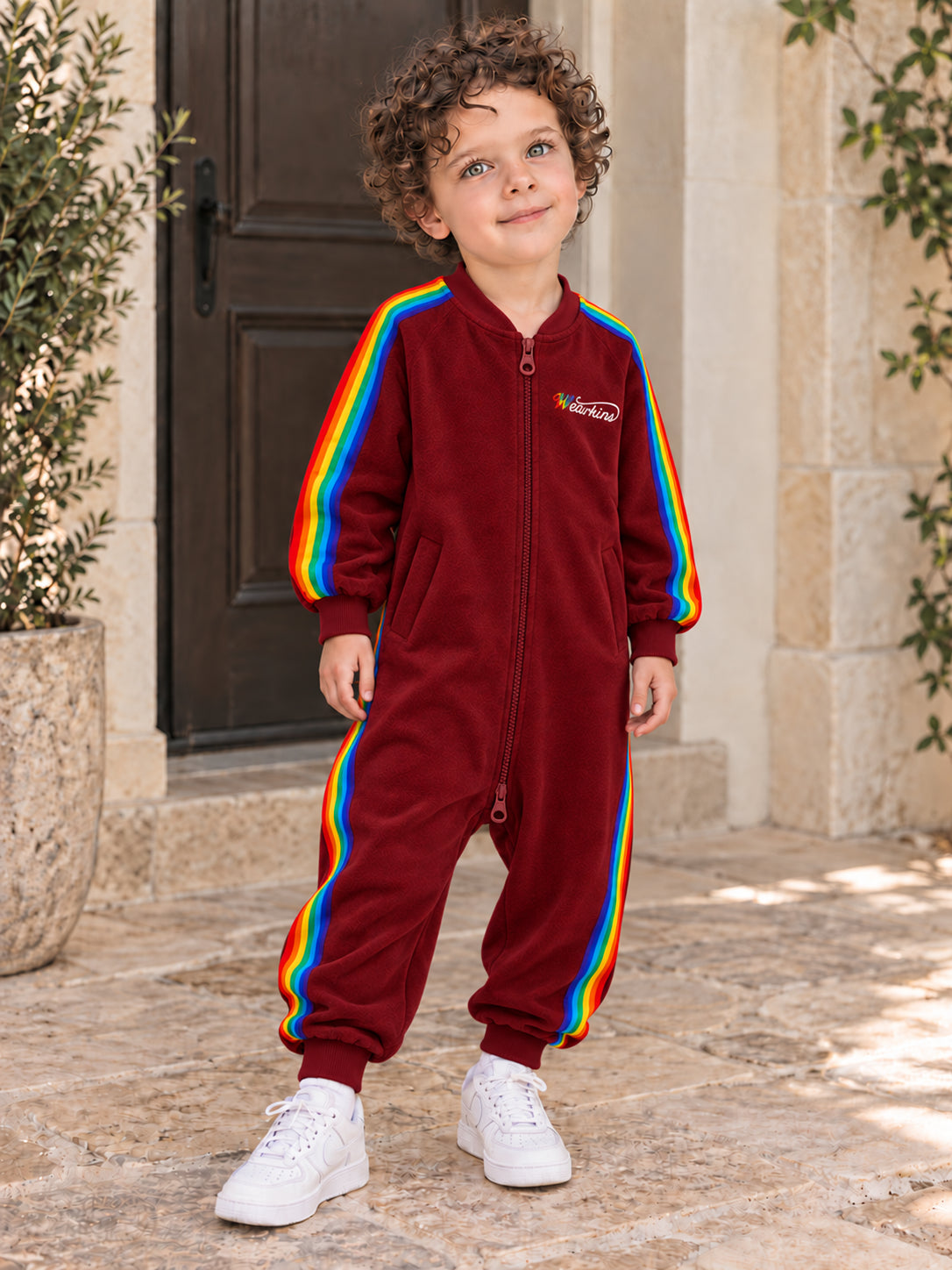 Child wearing a red rainbow-stripe onesie outdoors