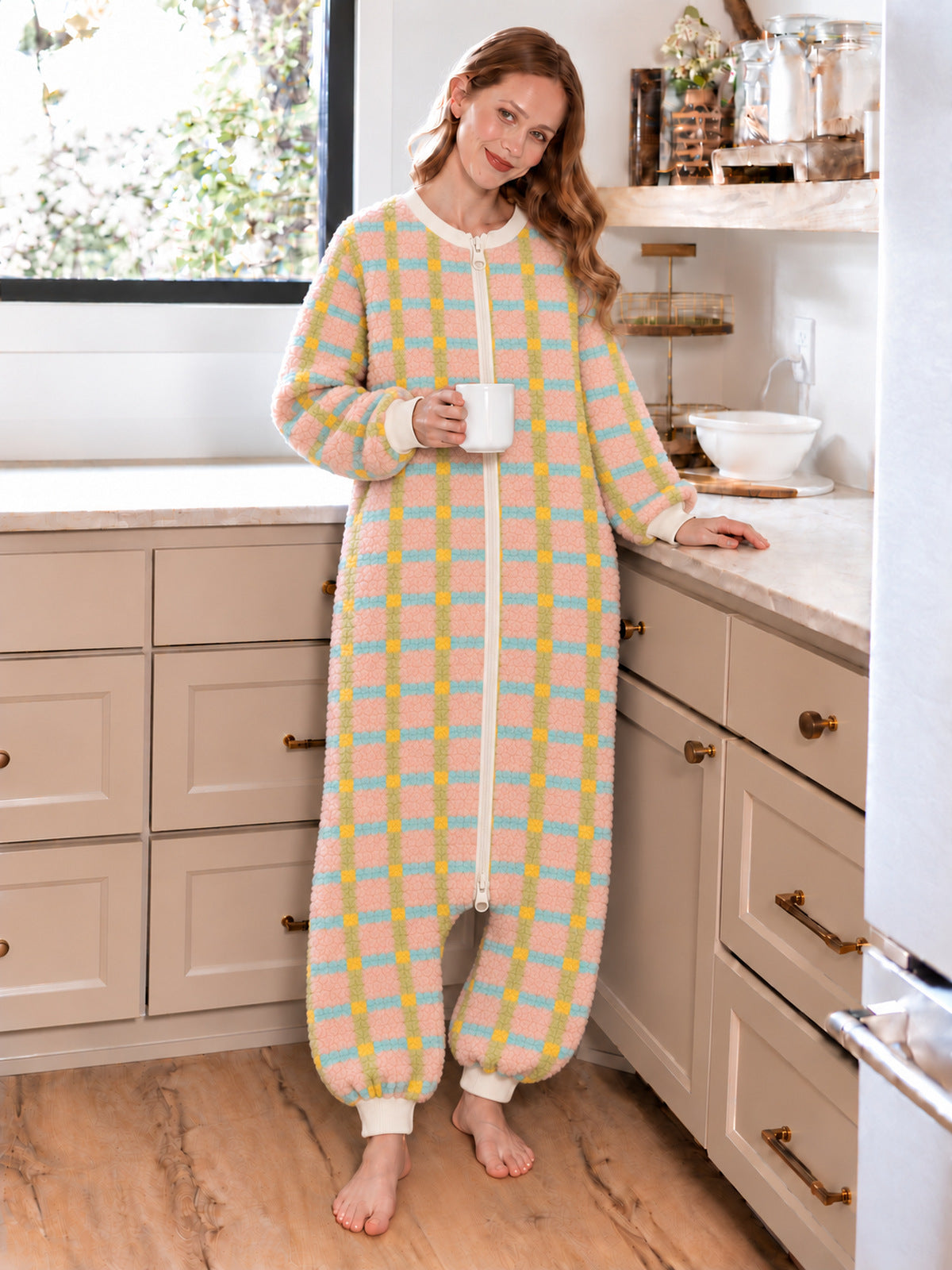 Adult model wearing the pastel plaid onesie while holding a mug in a sunlit kitchen