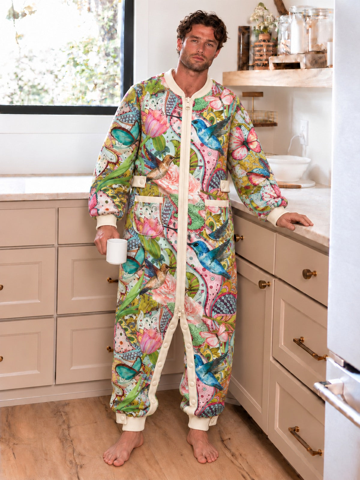 Man wearing the Hummingbird Garden floral onesie in a sunlit kitchen