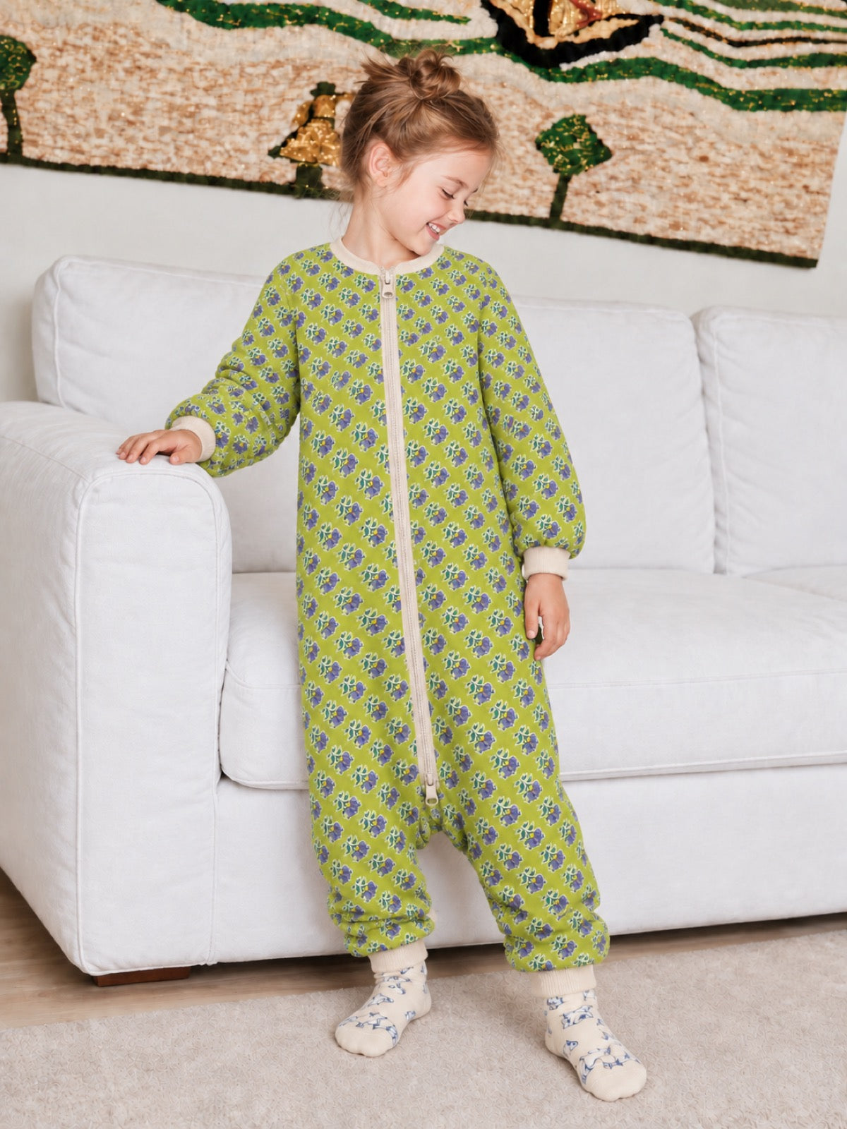 Girl wearing a lime-green floral onesie beside a white sofa